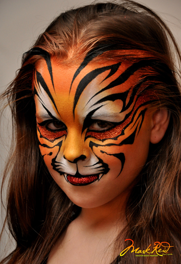 young girl in a full face painging of a tiger's face in orange and black